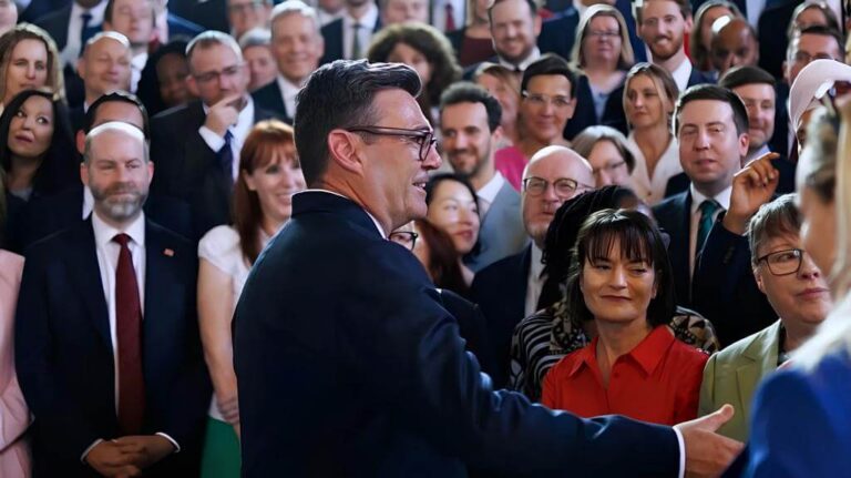 Andy Burnham, wearing glasses and a dark suit, engaging with a diverse group of professionals at a formal event.