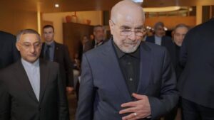 Iranian negotiator Mohammad Bagher Ghalibaf at a formal event, dressed in a dark suit and glasses, surrounded by officials.