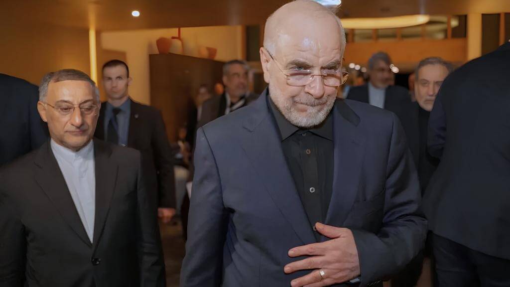 Iranian negotiator Mohammad Bagher Ghalibaf at a formal event, dressed in a dark suit and glasses, surrounded by officials.