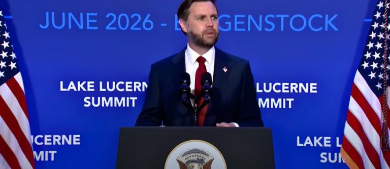U.S. Vice President JD Vance speaking at a podium during the Lake Lucerne Summit in June 2026, with American flags on either side.