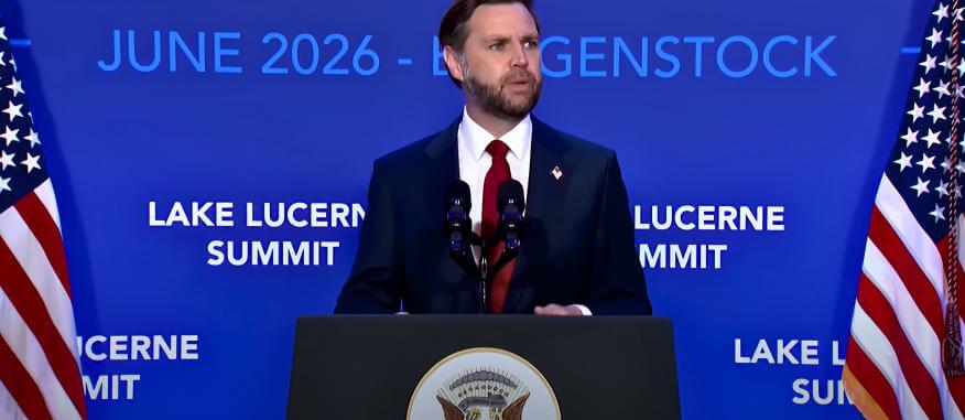 U.S. Vice President JD Vance speaking at a podium during the Lake Lucerne Summit in June 2026, with American flags on either side.