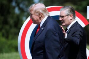 Former U.S. President Donald Trump standing outdoors with British Prime Minister Keir Starmer behind him, during a formal event with a red, white, and blue circular backdrop.